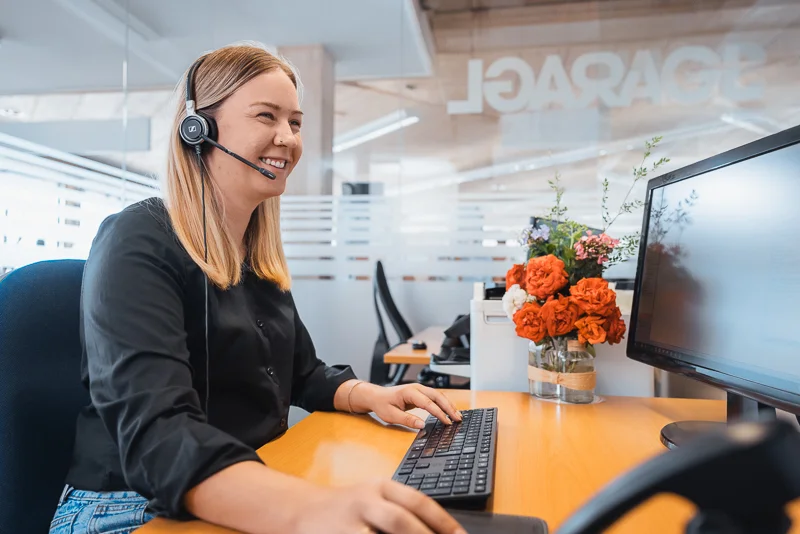 Servicemitarbeiterin mit Headset sitzt lächelnd bei der Arbeit vor ihrem Computer